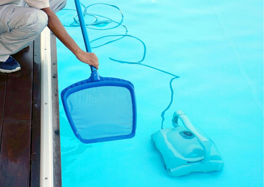 Pulizia piscina per riapertura primaverile con retino e robot pulitore in azione sul fondo della vasca