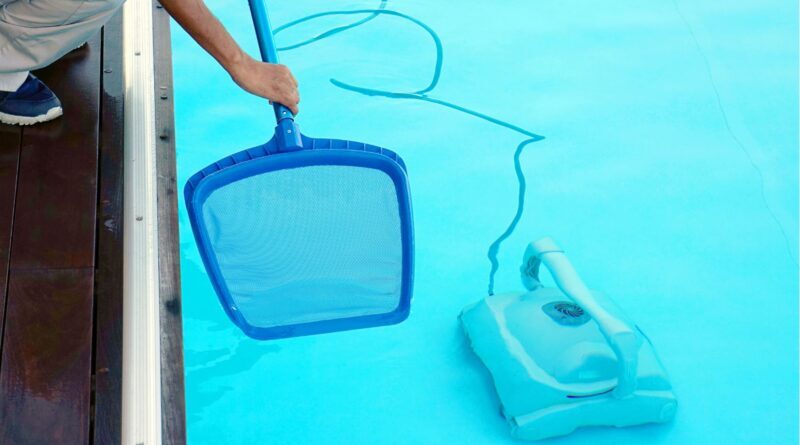 Pulizia piscina per riapertura primaverile con retino e robot pulitore in azione sul fondo della vasca